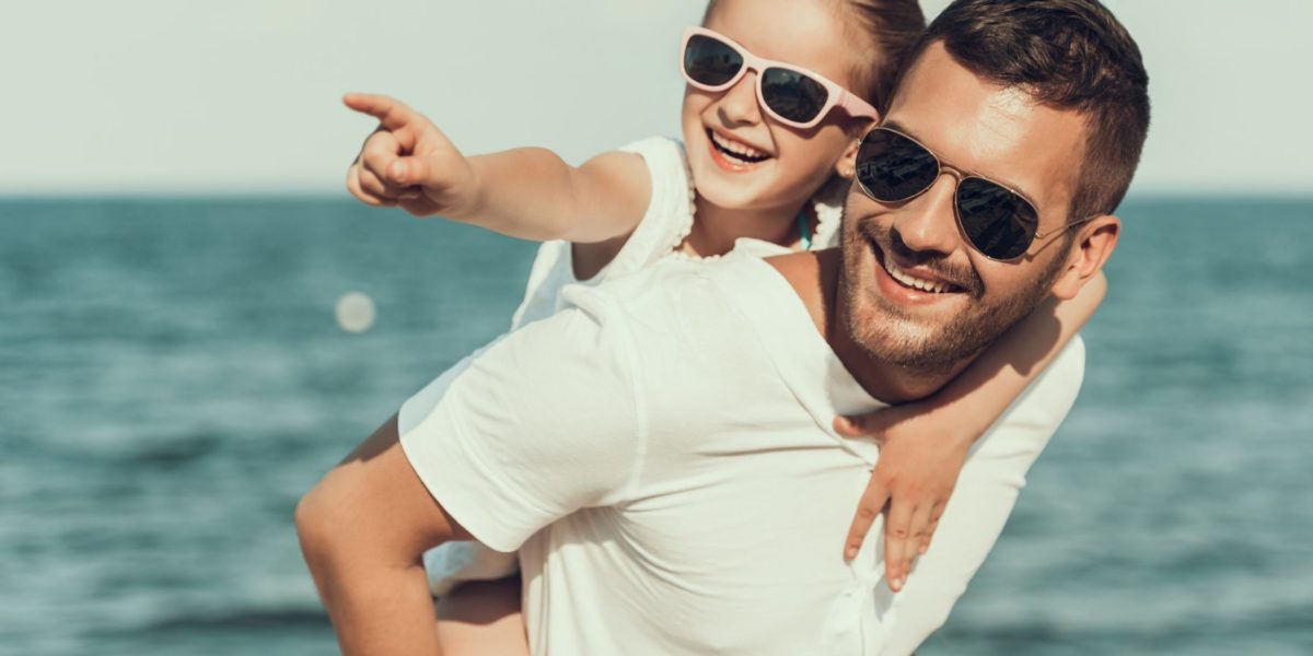 child wearing sunglasses by the water with her dad