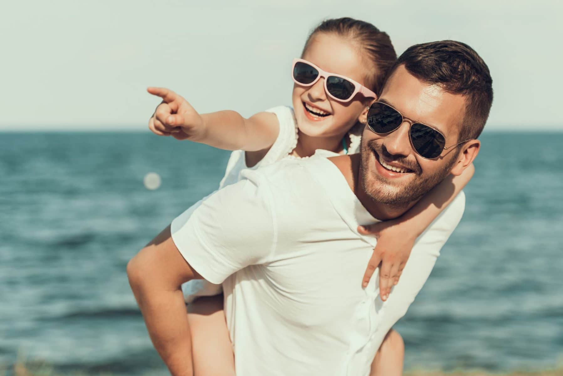 child wearing sunglasses by the water with her dad