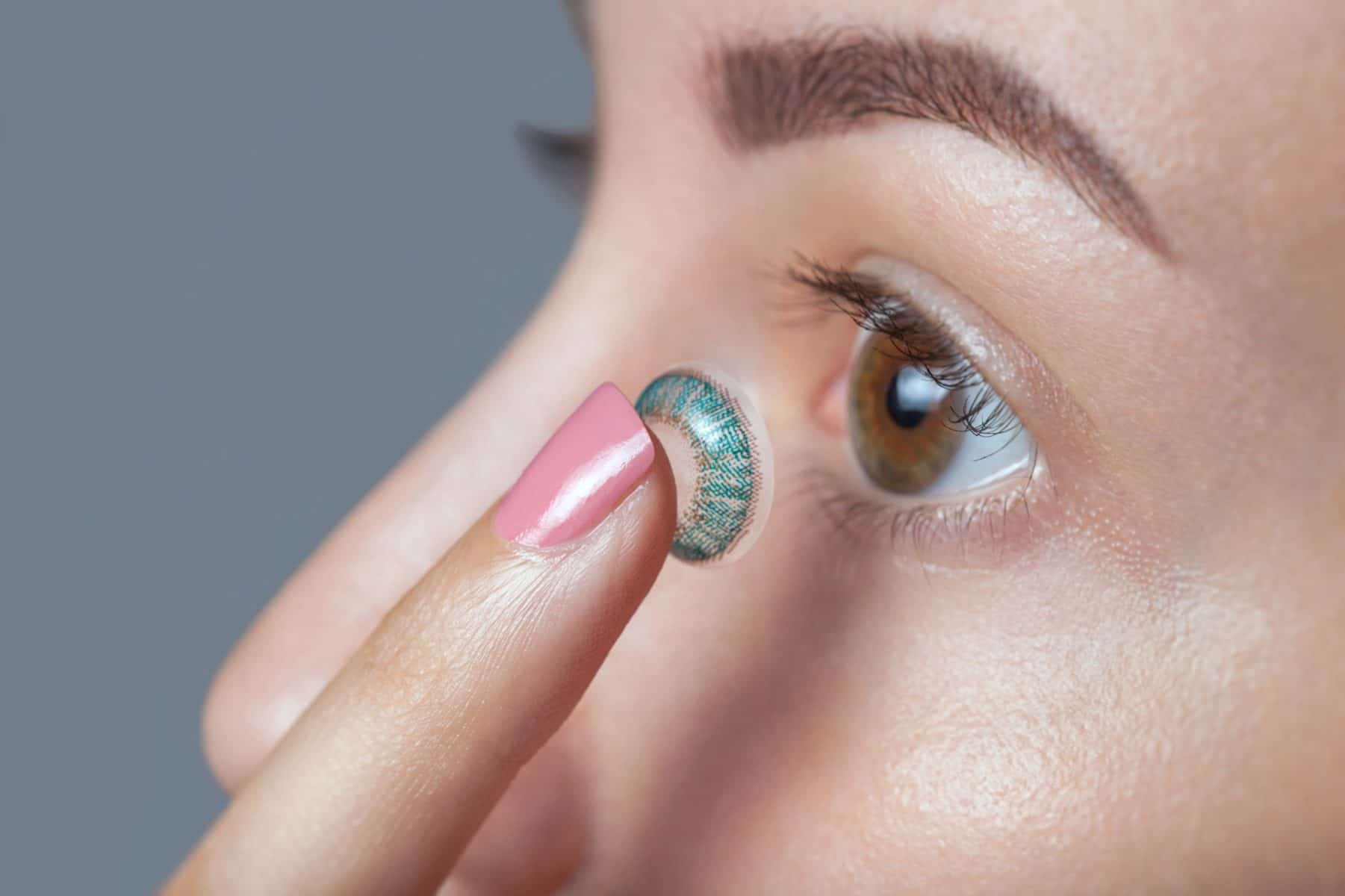 woman putting colored contact lens in her left eye