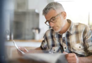 man using reading glasses to read newspaper